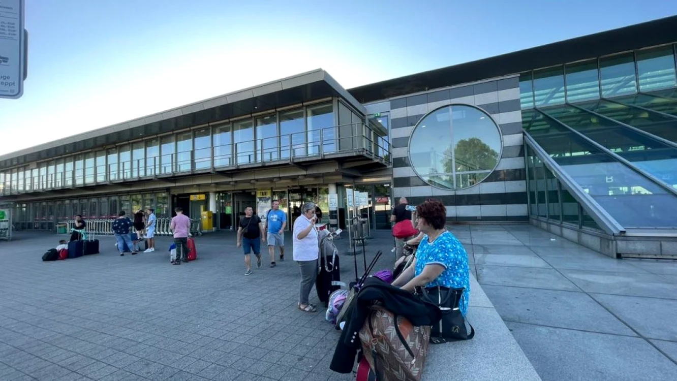 Oameni așezați pe bordura în fața unui aeroport