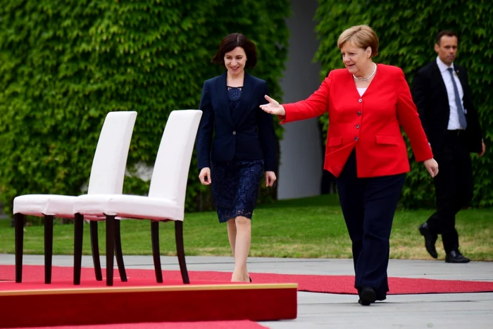 Angela Merkel invitând-o pe Maia Sandu să se aşeze pe scaun pentru ascultarea imnurilor FOTO EPA-EFE