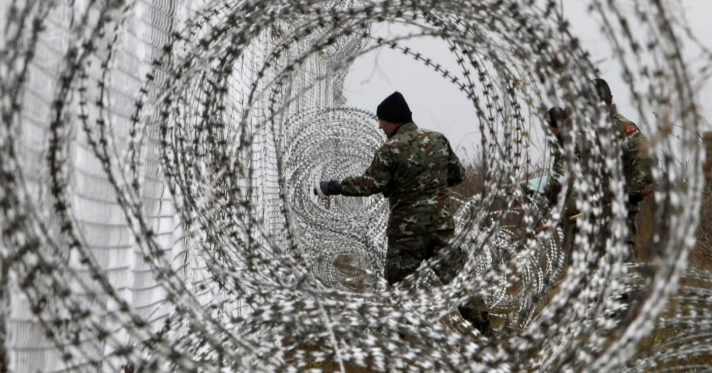 Un soldat al armatei macedonene întinde un gard de sârmă ghimpată la graniţa dintre Macedonia şi Grecia