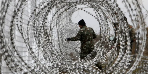 Un soldat al armatei macedonene întinde un gard de sârmă ghimpată la graniţa dintre Macedonia şi Grecia