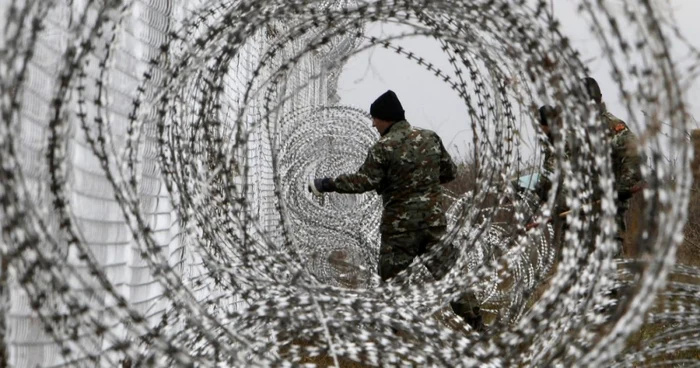 Un soldat al armatei macedonene întinde un gard de sârmă ghimpată la graniţa dintre Macedonia şi Grecia
