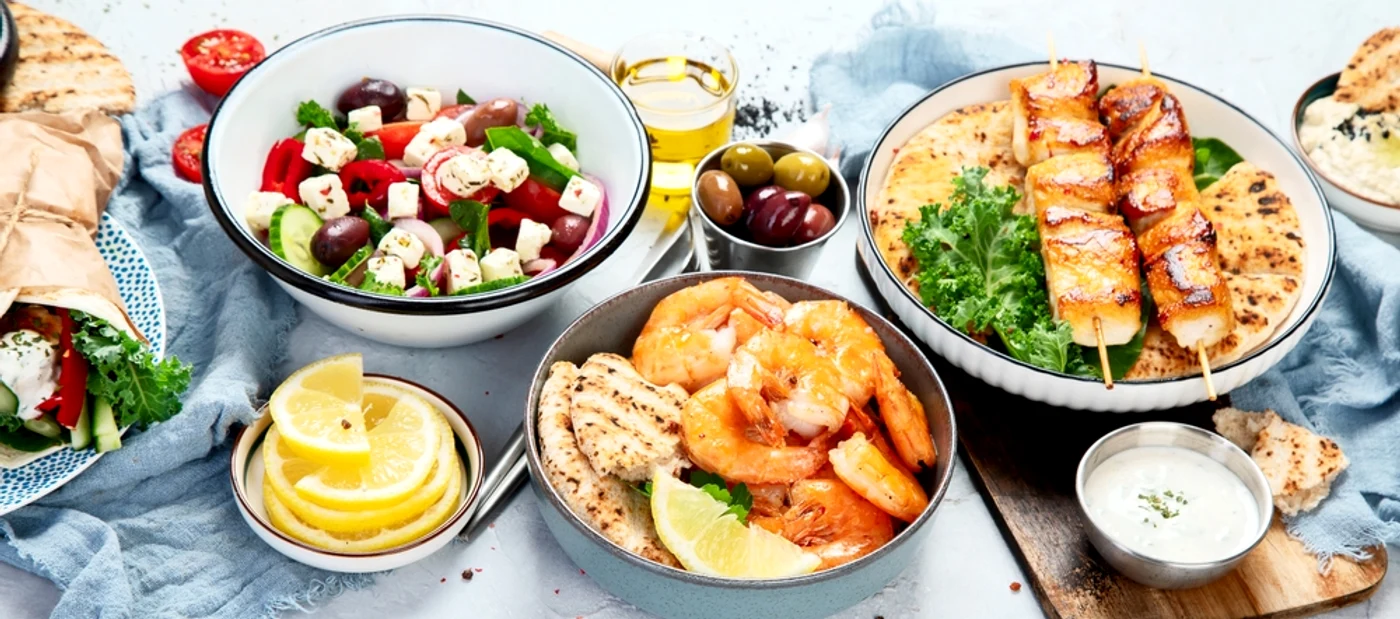 Masă cu farfurii cu mâncăruri tradiționale grecești: creveți, salată grecească, souvlaki