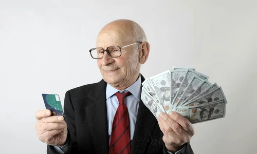 un barbat cu ochelari tine in mana drapta un card de credit si in mana stanga bancnote dolari jpg