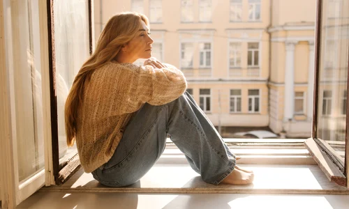 sad fairskinned adult woman blonde warm sweater jeans sitting windowsill sunny day mood concept jpg