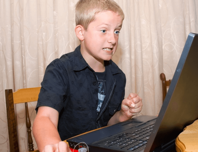 Copil care se uită furios la ecranul laptopului