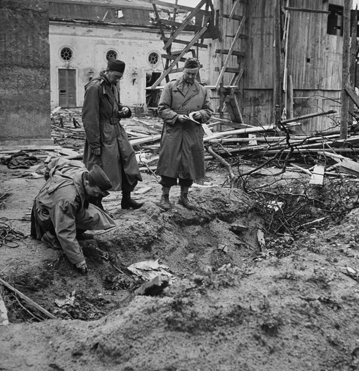 Soldaţi Aliaţi examinând locul unde au fost incinerate trupurile lui Adolf Hitler şi al Evei Braun. Cele două corpuri au fost aşezate unul lângă
altul,  pe o porţiune de pământ drept,  liber,  nisipos,  la numai trei metri de uşa buncărului 