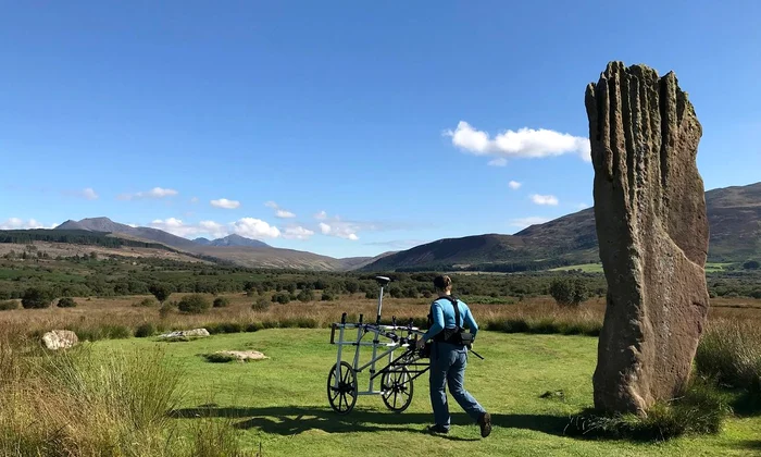 Un cercetător folosește echipament pentru a detecta anomalii sub turbă la Machrie Moor (© Historic Environment Scotland)