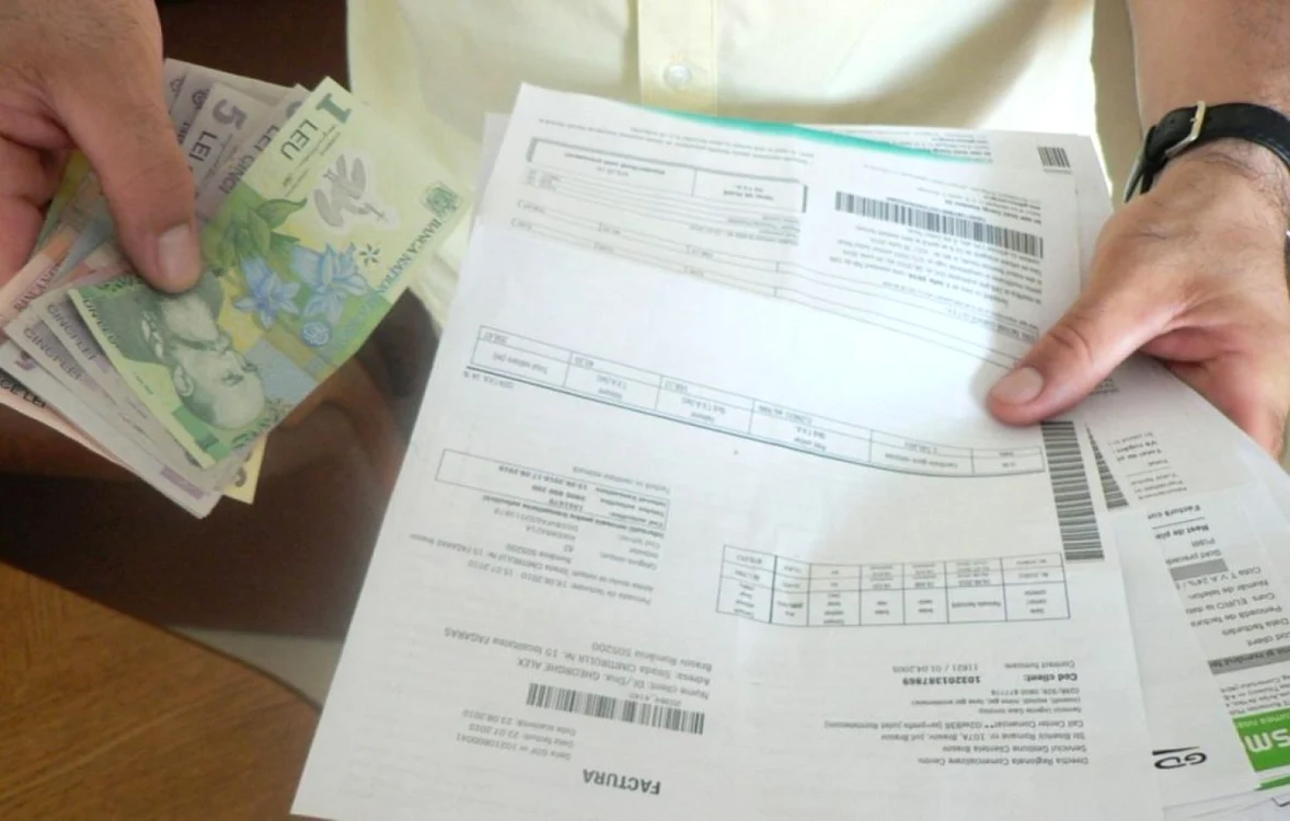Cineva ține în mână mai multe facturi, iar în cealaltă bani