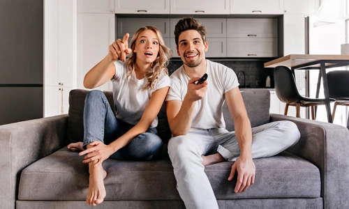 curious couple sitting grey sofa indoor portrait man woman watch tv jpg