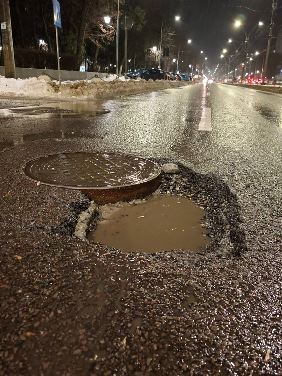 Groapă adâncă în asfalt lângă un capac de canalizare
