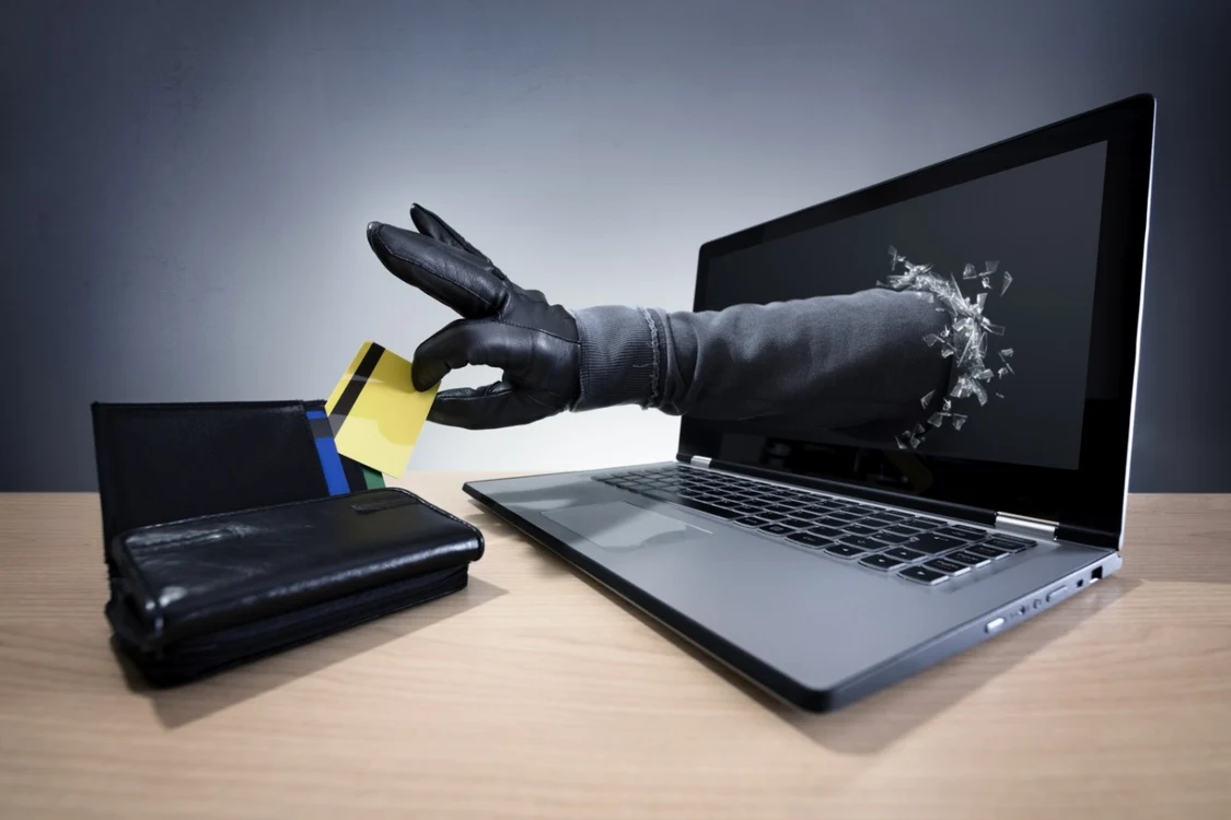 O mână iese dintr-un laptop și fură un card din portofel, imaginea sugerând un atac cibernetic