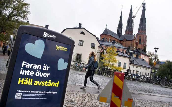 O femeie trece pe lângă un tomberon pe care e afişat mesajul de atenţionare legat de pandemia de COVID-19: „Pericolul nu a trecut. Păstraţi distanţa“, în Uppsala, Suedia Foto EPA EFE