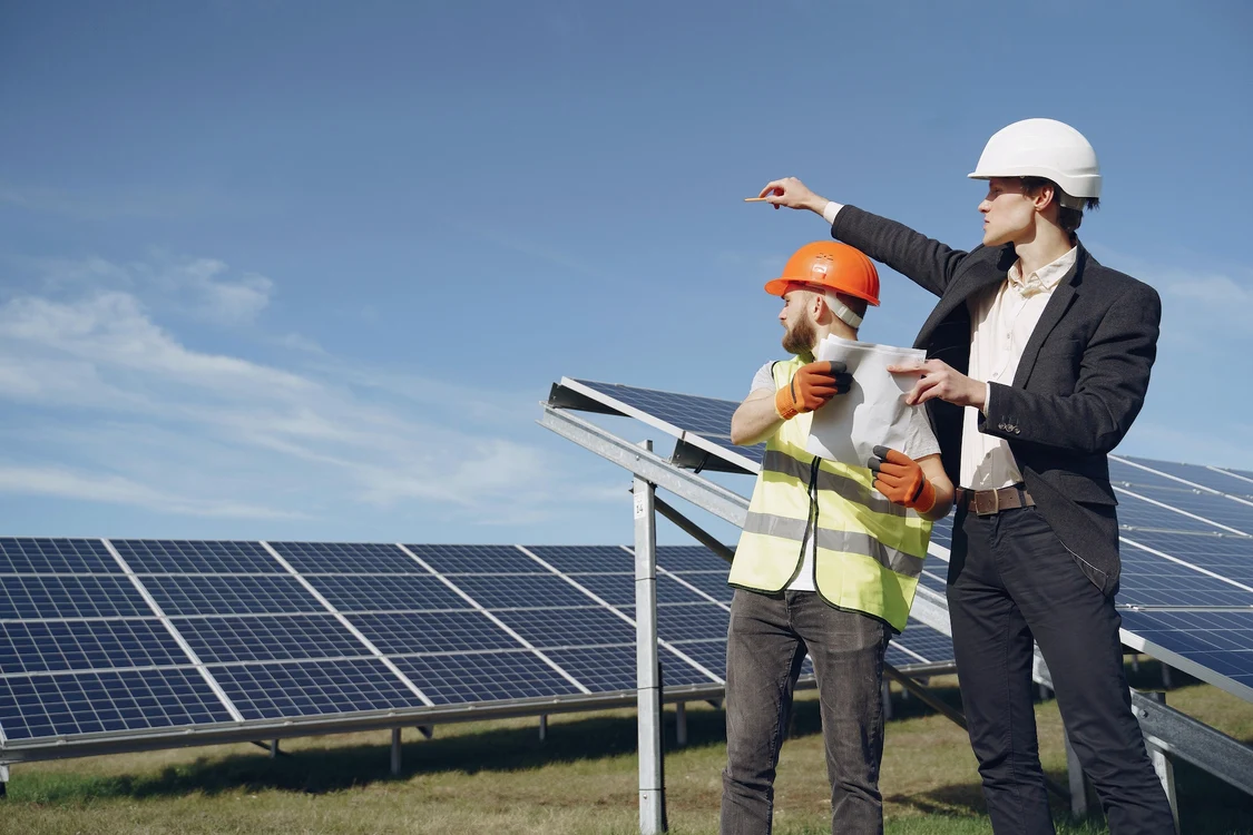 Doi constructori privesc în zare lângă un parc de panouri fotovoltaice