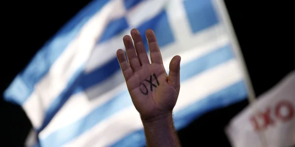 Un protestatar are scris pe mana cuvantul nu in timp ce un steag grec flutura in spate. Oamenii s-au adunat in Atena pentru a demonstra impotriva referendumului de duminica in care se cere ca grecii sa accepte mai multa austeritate pentru a primii