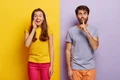 positive young female whispers secret with glad expression serious guy keeps fore finger lips jpg