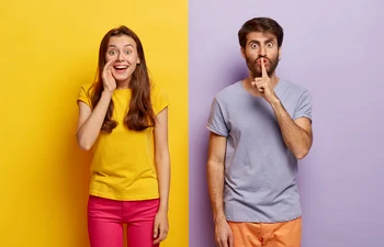 positive young female whispers secret with glad expression serious guy keeps fore finger lips jpg