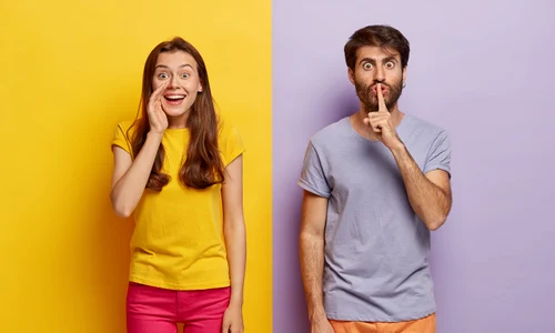 positive young female whispers secret with glad expression serious guy keeps fore finger lips jpg