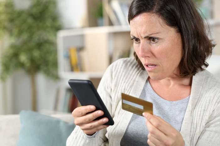 O femeie se uită îngrozită la telefon care îi arată cum i-au fost furați bani de pe card