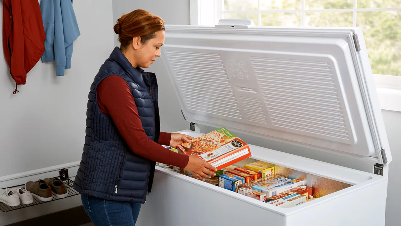 Femeie scoțând alimente dintr-o ladă frigorifică plină cu produse congelate Foto Amana.com