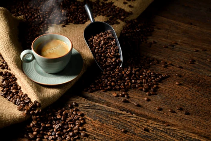 O ceașcă de cafea aburindă în mijlocul unor boabe de cafea