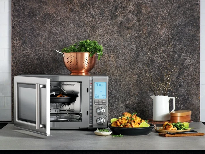 Un cuptor cu microunde lângă care se află o tavă cu mâncare apetisantă Sursă Breville com
