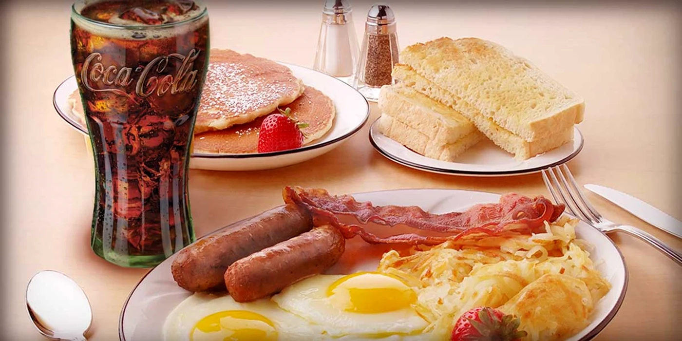 O masă pe care sunt așezate farfurii cu mâncare sărată și dulce, sare și zahăr și suc Coke Solutions