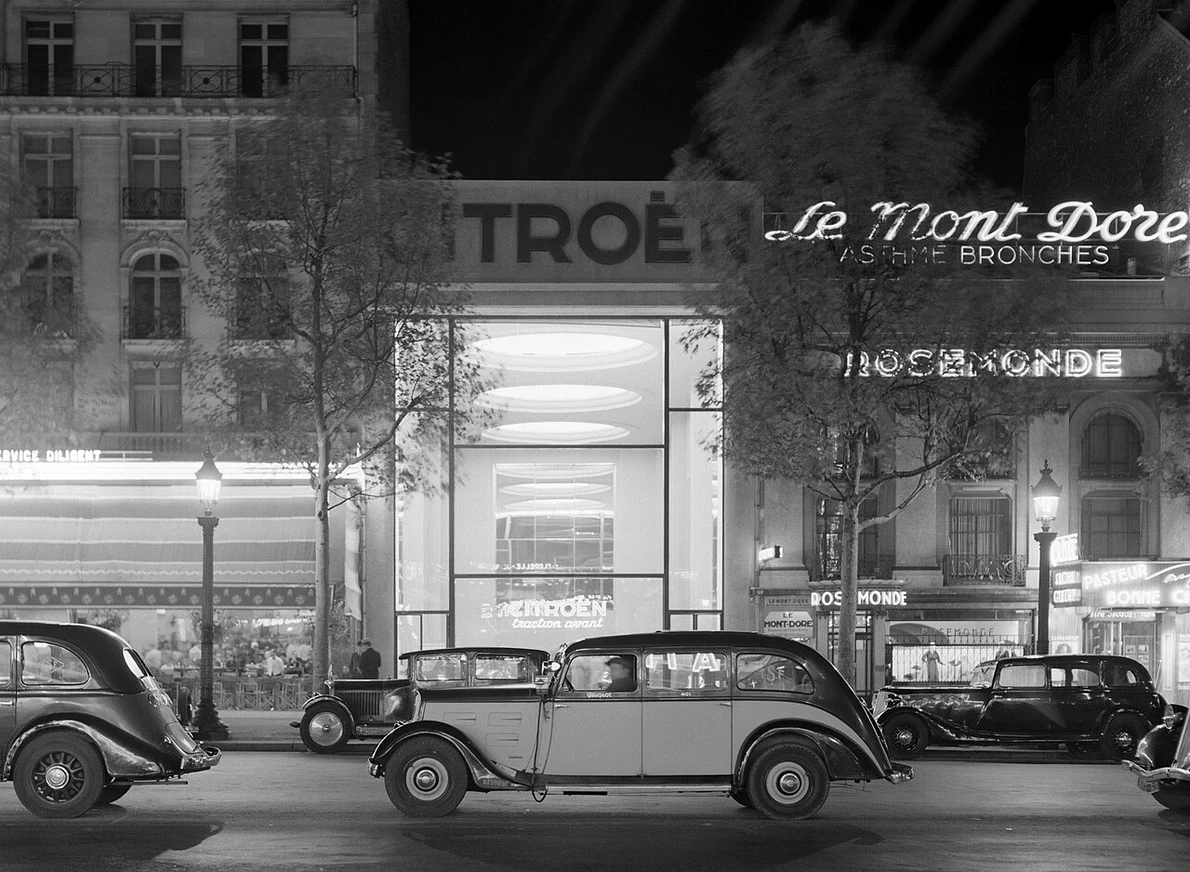 Mașini pe Champs-Élysées, cu showroom-ul Citroën iluminat în fundal, în perioada interbelică. Fotografie de Willem van de Poll (© Nationaal Archief)
