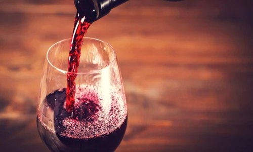 Pouring red wine into the glass against wooden background jpeg