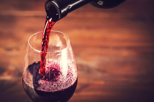 Pouring red wine into the glass against wooden background jpeg