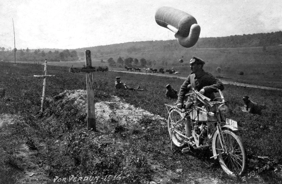 Un motociclist studiază o crucea unui mormânt,  iar în spatele său un balon se pregăteşte să se ridice de la sol. Pe cruce scrie în Germană: 