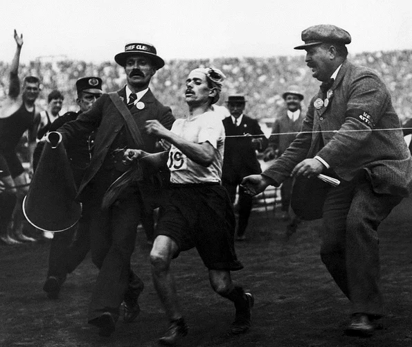 Maratonistul italian Dorando Pietri, ajutat să treacă linia de sosire la Olimpiada de la Londra din 1908 (© Wikimedia Commons)