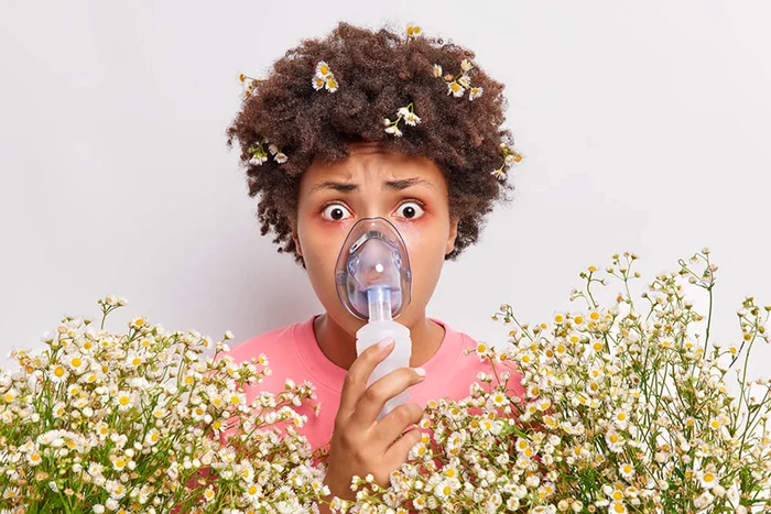 Femeie cu mască pentru inhalații, înconjurată de flori de mușețel Foto Premier Allergy&Asthma