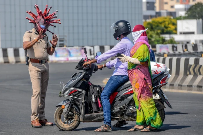 Un polițist indian poartă o cască în formă de coronaviurs, pentru a convinge oamenii să stea în casăFoto AFP