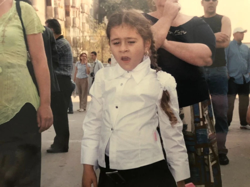 Nicole Cherry în copilărie, elevă, pe stradă, îmbrăcată în cămașă albă și fustiță